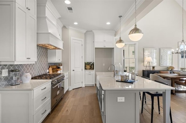 kitchen featuring tasteful backsplash, stainless steel stove, white cabinetry, wood finished floors, and premium range hood