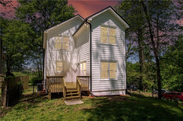 back house at dusk with a yard, central AC, and a wooden deck