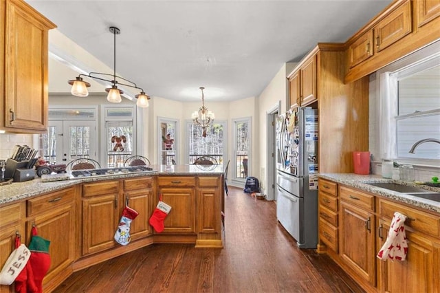 kitchen with decorative light fixtures, a notable chandelier, sink, stainless steel refrigerator, and light stone counters