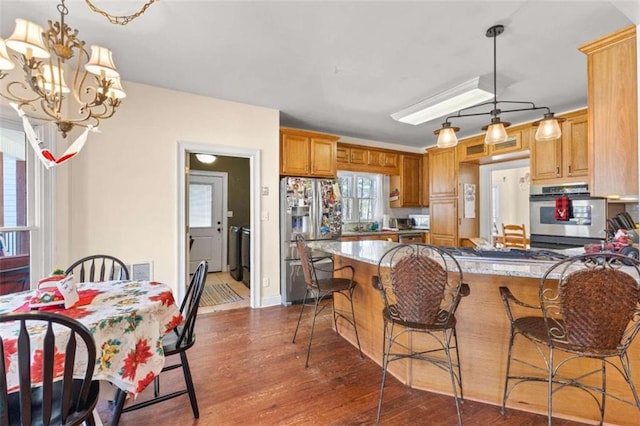 kitchen featuring kitchen peninsula, dark wood-type flooring, a kitchen breakfast bar, stainless steel appliances, and a chandelier