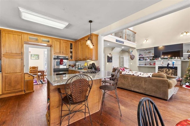 kitchen with appliances with stainless steel finishes, dark wood-type flooring, hanging light fixtures, light stone counters, and a breakfast bar