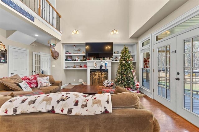 living room featuring wood-type flooring, a high ceiling, built in shelves, and french doors