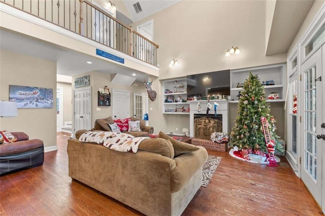 living room with a brick fireplace, built in features, a towering ceiling, and hardwood / wood-style floors