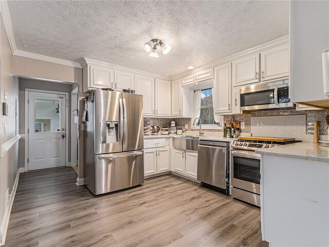 kitchen with appliances with stainless steel finishes, tasteful backsplash, a sink, light wood-style floors, and white cabinetry
