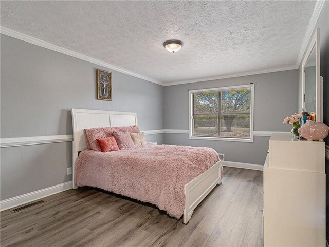 bedroom with visible vents, ornamental molding, baseboards, and wood finished floors