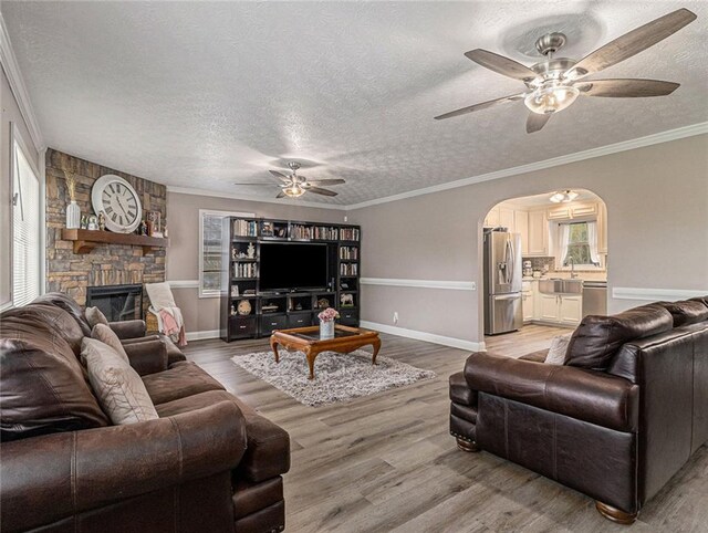 living room featuring a ceiling fan, a textured ceiling, arched walkways, and light wood-style flooring