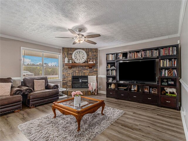 living area featuring a ceiling fan, a textured ceiling, crown molding, a fireplace, and wood finished floors