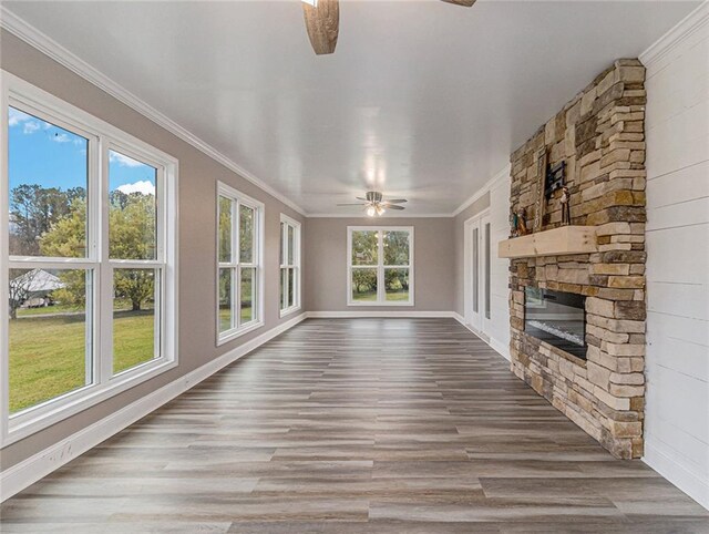 unfurnished living room featuring crown molding, wood finished floors, a fireplace, baseboards, and a ceiling fan