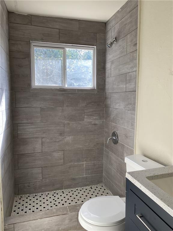 bathroom with tiled shower, vanity, and toilet