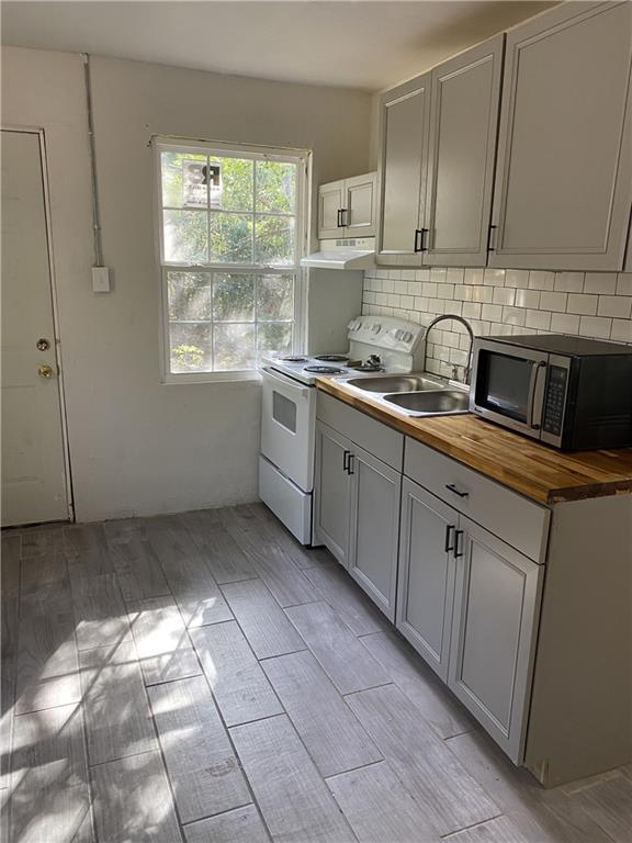 kitchen with stainless steel microwave, white range with electric stovetop, wooden counters, extractor fan, and a sink