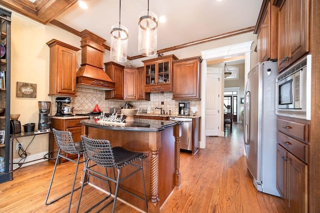 kitchen featuring decorative light fixtures, light hardwood / wood-style floors, custom range hood, stainless steel appliances, and a center island