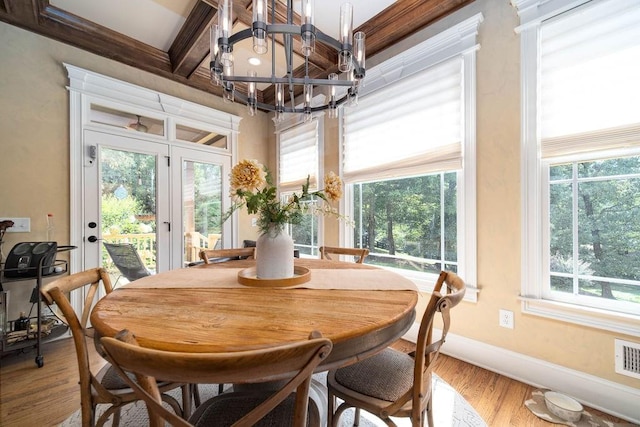 dining space with an inviting chandelier, beam ceiling, light hardwood / wood-style floors, and french doors