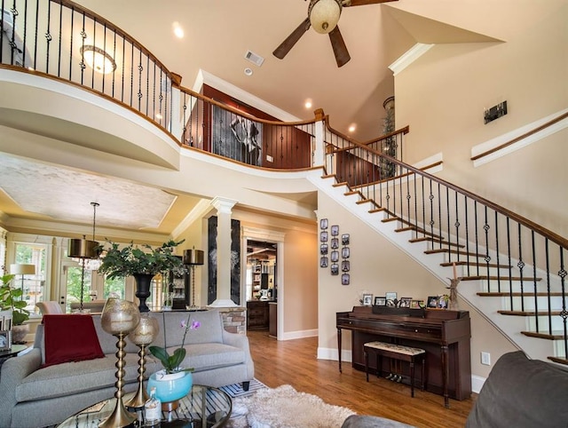 living room with ornate columns, dark hardwood / wood-style floors, ceiling fan, ornamental molding, and a high ceiling