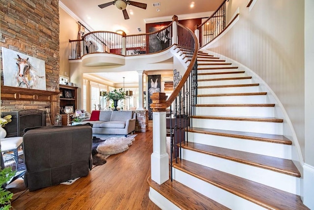 stairs featuring a high ceiling, dark hardwood / wood-style floors, ceiling fan, a stone fireplace, and ornamental molding