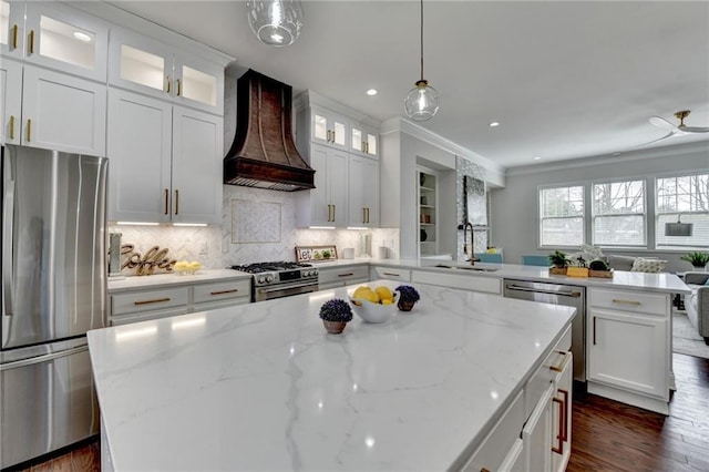 kitchen with custom exhaust hood, stainless steel appliances, a sink, a kitchen island, and a peninsula