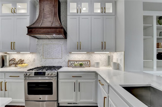 kitchen with premium range hood, stainless steel gas range oven, backsplash, and white cabinetry