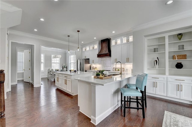 kitchen with custom range hood, a kitchen island, ornamental molding, freestanding refrigerator, and a sink