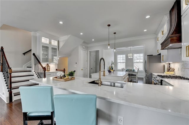 kitchen with decorative backsplash, dark wood-style floors, ornamental molding, custom exhaust hood, and a sink