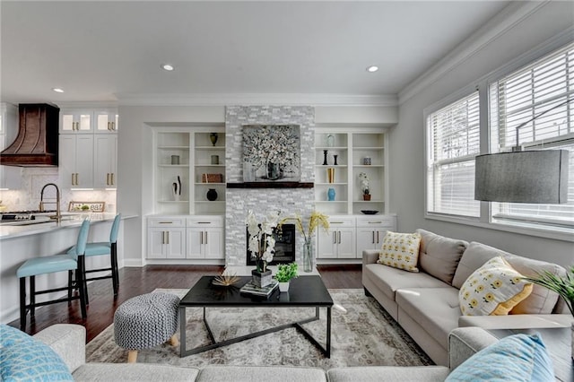 living room featuring dark wood-type flooring, recessed lighting, crown molding, and a stone fireplace