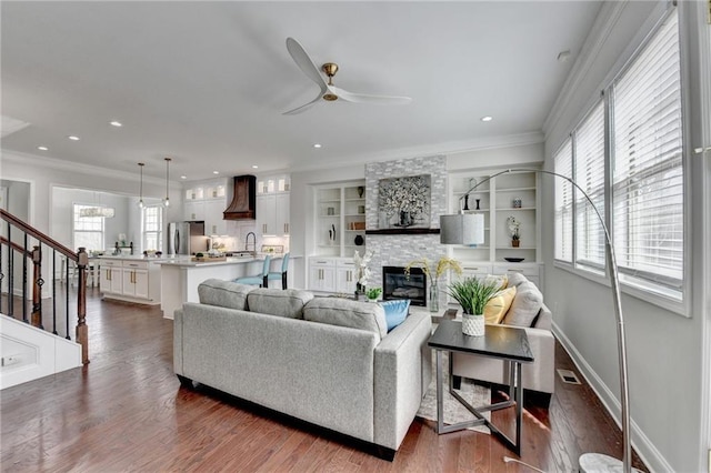 living area featuring a fireplace, ornamental molding, dark wood finished floors, and a ceiling fan