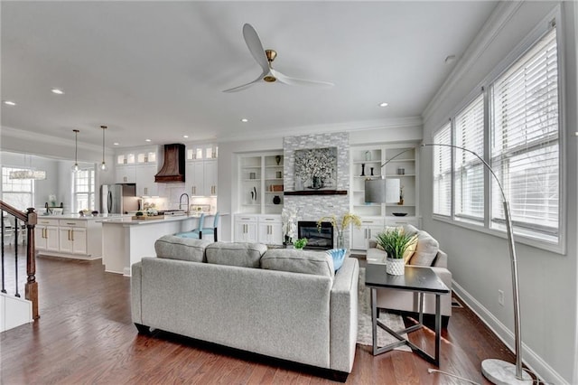 living room with a fireplace, a ceiling fan, stairs, dark wood finished floors, and crown molding