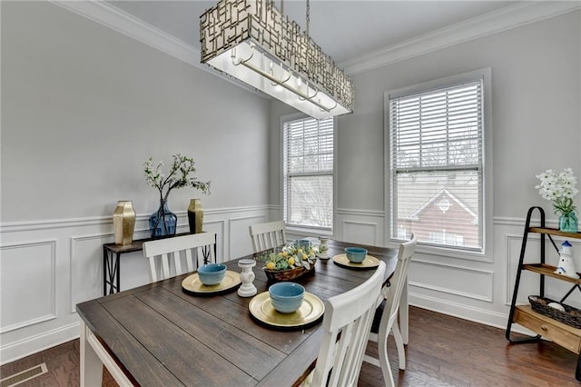 dining room featuring visible vents, a decorative wall, ornamental molding, dark wood-type flooring, and wainscoting