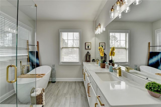 full bath featuring double vanity, a soaking tub, a sink, wood finished floors, and baseboards