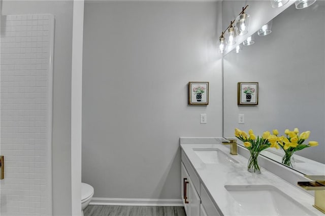 bathroom featuring toilet, wood finished floors, a sink, baseboards, and double vanity