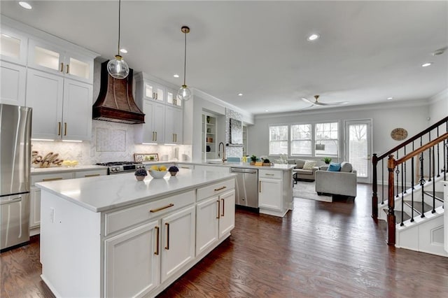 kitchen featuring appliances with stainless steel finishes, open floor plan, a sink, premium range hood, and a peninsula