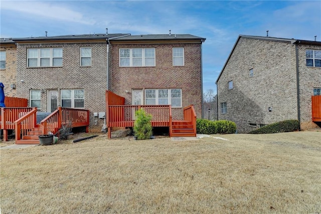 rear view of property with brick siding, a lawn, and a wooden deck