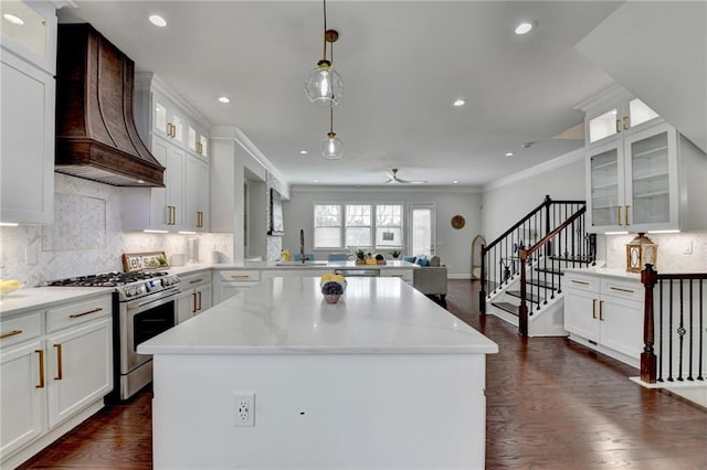 kitchen featuring custom range hood, ornamental molding, stainless steel gas stove, white cabinets, and a peninsula