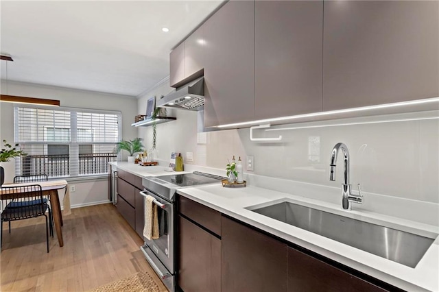 kitchen featuring sink, wall chimney range hood, dark brown cabinets, stainless steel range with electric cooktop, and light wood-type flooring