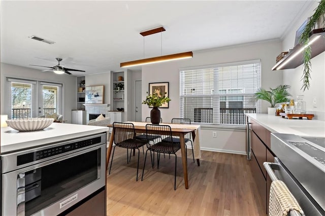 kitchen featuring ceiling fan, stainless steel oven, hanging light fixtures, crown molding, and light wood-type flooring