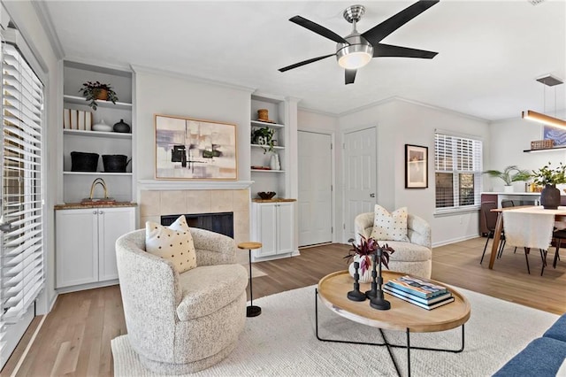 living room featuring ceiling fan, light wood-type flooring, crown molding, and a tile fireplace