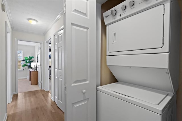 clothes washing area featuring light wood-type flooring, crown molding, and stacked washer / drying machine