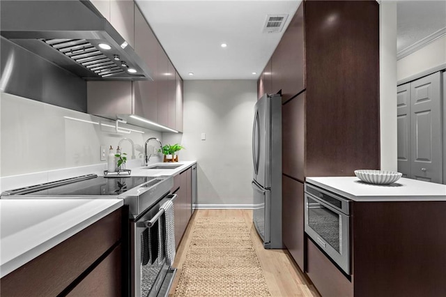 kitchen with sink, wall chimney exhaust hood, stainless steel appliances, light wood-type flooring, and ornamental molding