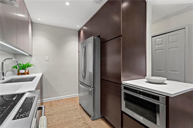 kitchen featuring oven, sink, stainless steel fridge, light wood-type flooring, and dark brown cabinets