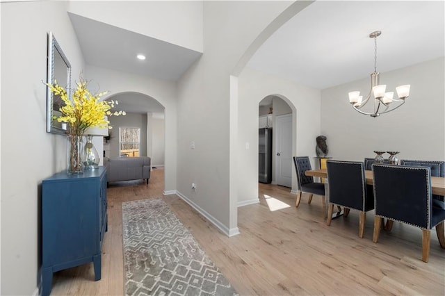 interior space featuring a notable chandelier, light wood-style flooring, recessed lighting, arched walkways, and baseboards