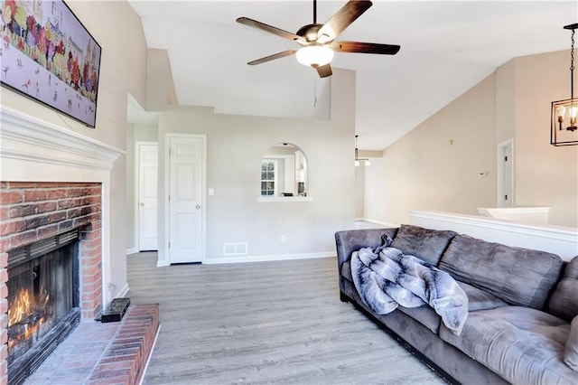 living room featuring hardwood / wood-style floors, ceiling fan with notable chandelier, lofted ceiling, and a fireplace