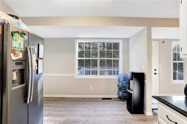 kitchen with stainless steel refrigerator with ice dispenser, light wood-type flooring, and white cabinetry