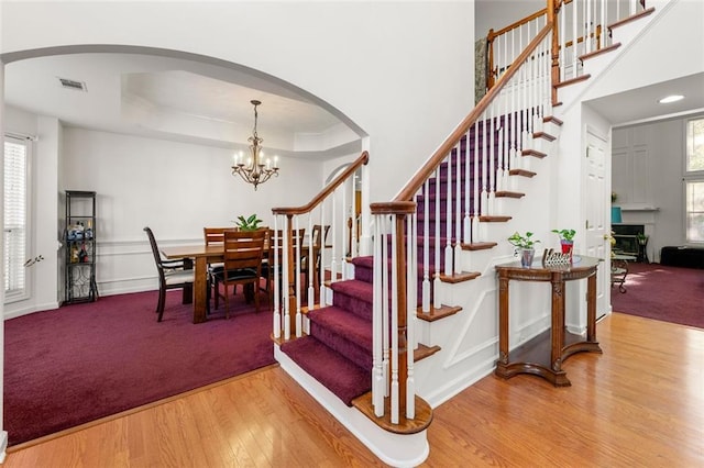 staircase featuring hardwood / wood-style floors, a raised ceiling, a chandelier, and plenty of natural light