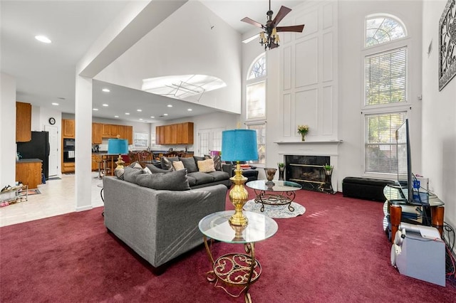 carpeted living room featuring a large fireplace, a high ceiling, and ceiling fan