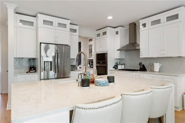 kitchen featuring white cabinetry, stainless steel fridge, a breakfast bar, and wall chimney exhaust hood