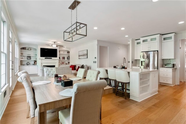 dining space with ceiling fan, light hardwood / wood-style floors, ornamental molding, and built in shelves