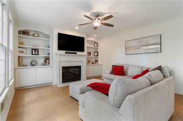 living room featuring built in shelves, ceiling fan, crown molding, and light hardwood / wood-style flooring