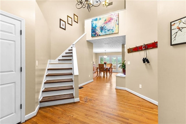 stairs with a chandelier, visible vents, baseboards, and wood finished floors