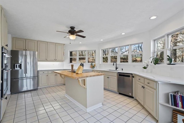 kitchen featuring stainless steel appliances, light tile patterned flooring, a sink, wood counters, and a textured ceiling