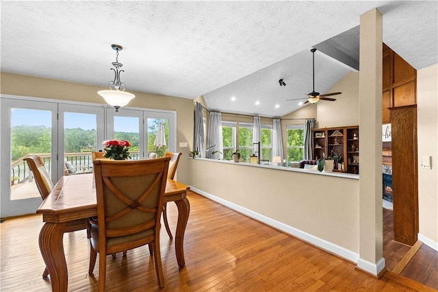 dining room featuring baseboards, a glass covered fireplace, wood finished floors, vaulted ceiling, and a textured ceiling