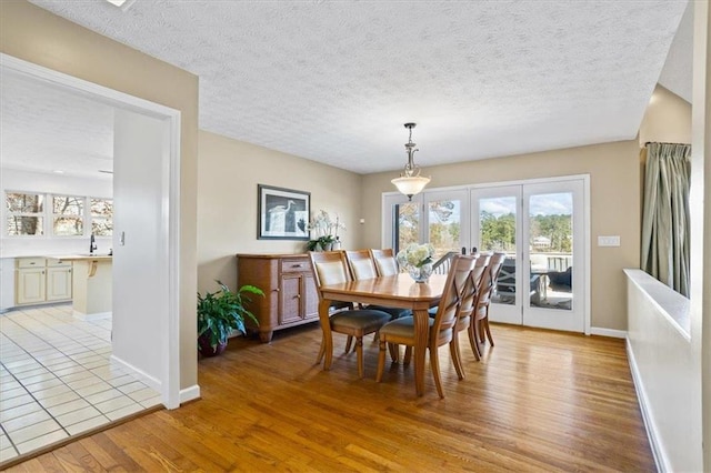 dining space with light wood-style flooring, baseboards, a textured ceiling, and french doors