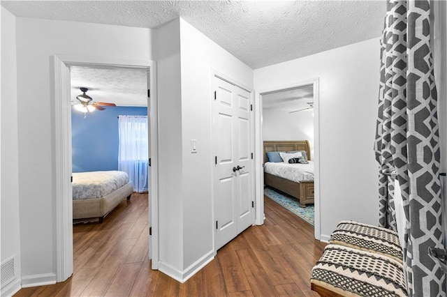 hallway with dark wood-style flooring, a textured ceiling, and baseboards